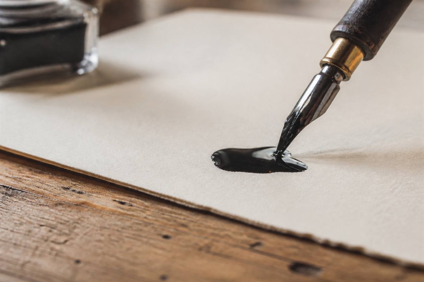 Calligraphy nib touching a pool of black ink on textured paper